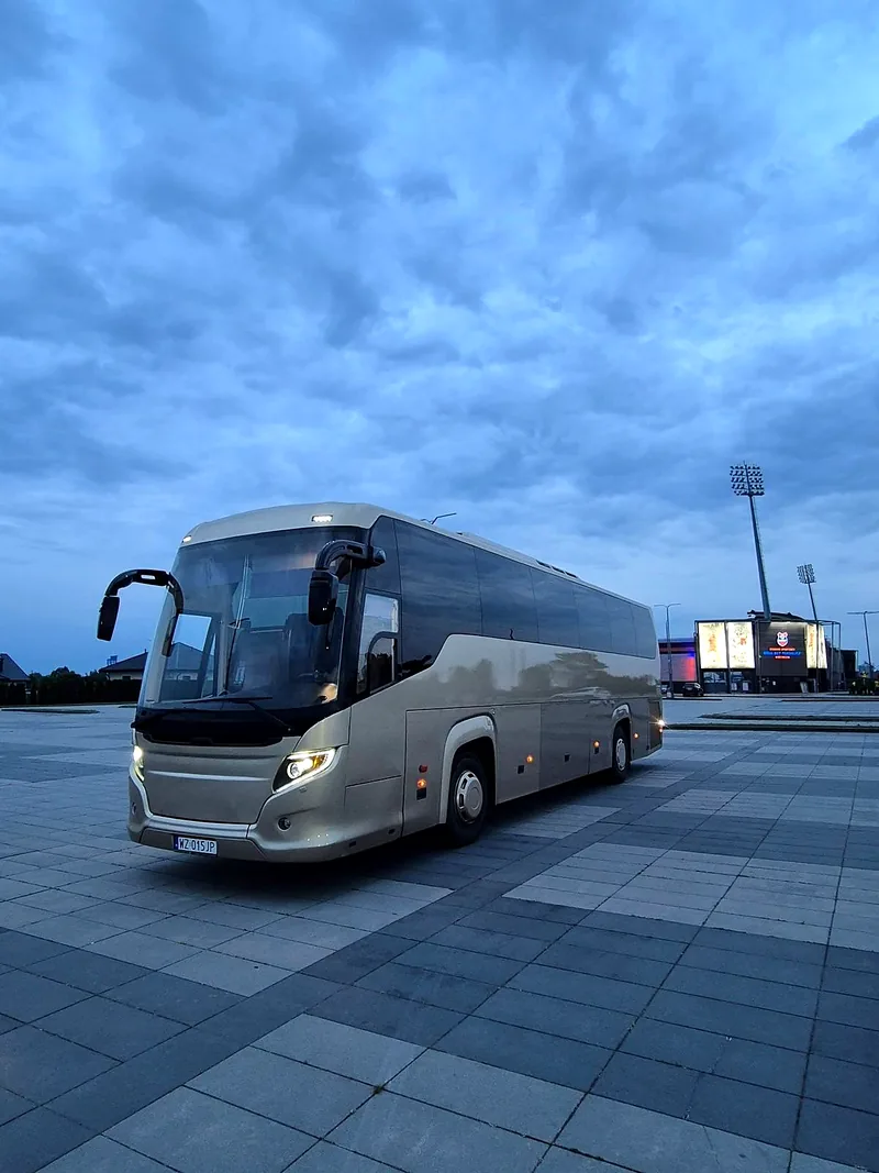 Autokar Scania Touring wieczorem pod stadionem, z włączonymi światłami
