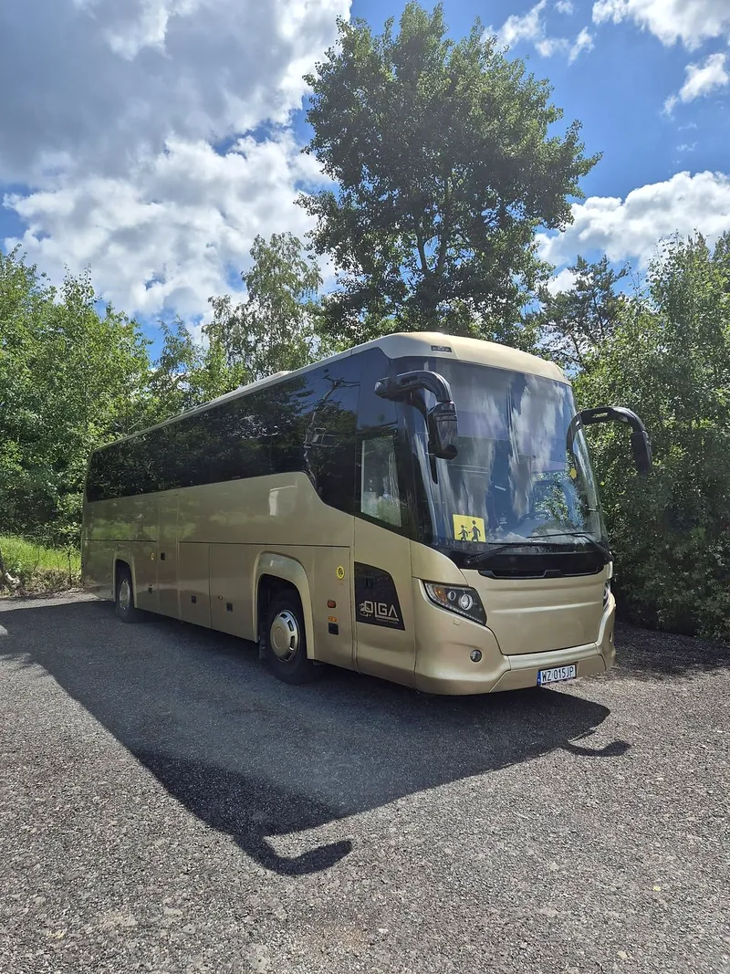 Złoty autokar Scania Touring floty OLGA na tle drzew i nieba